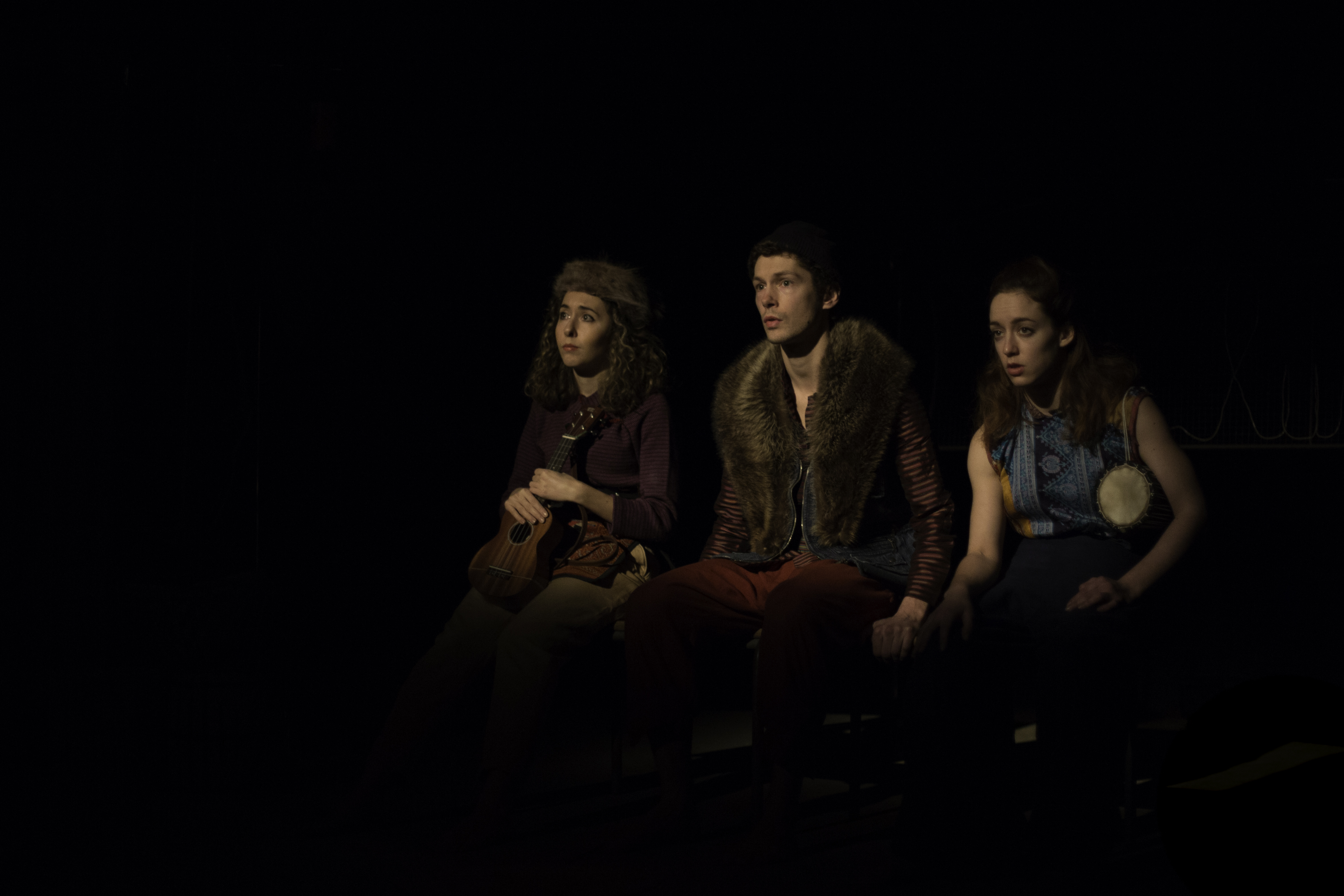 Three performers knelt, looking ahead, concerned