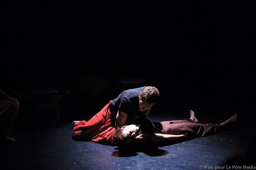 Performer holding unconscious performer in arms, in harsh spotlight