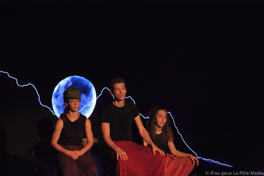 Performers sat looking content with moon and lightning behind them
