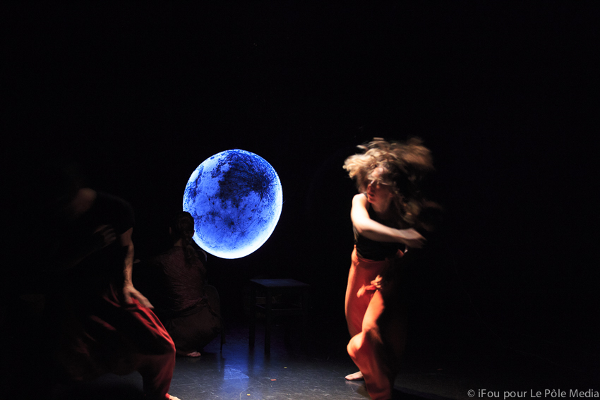 Performers blurry from physical theatre with moon in background