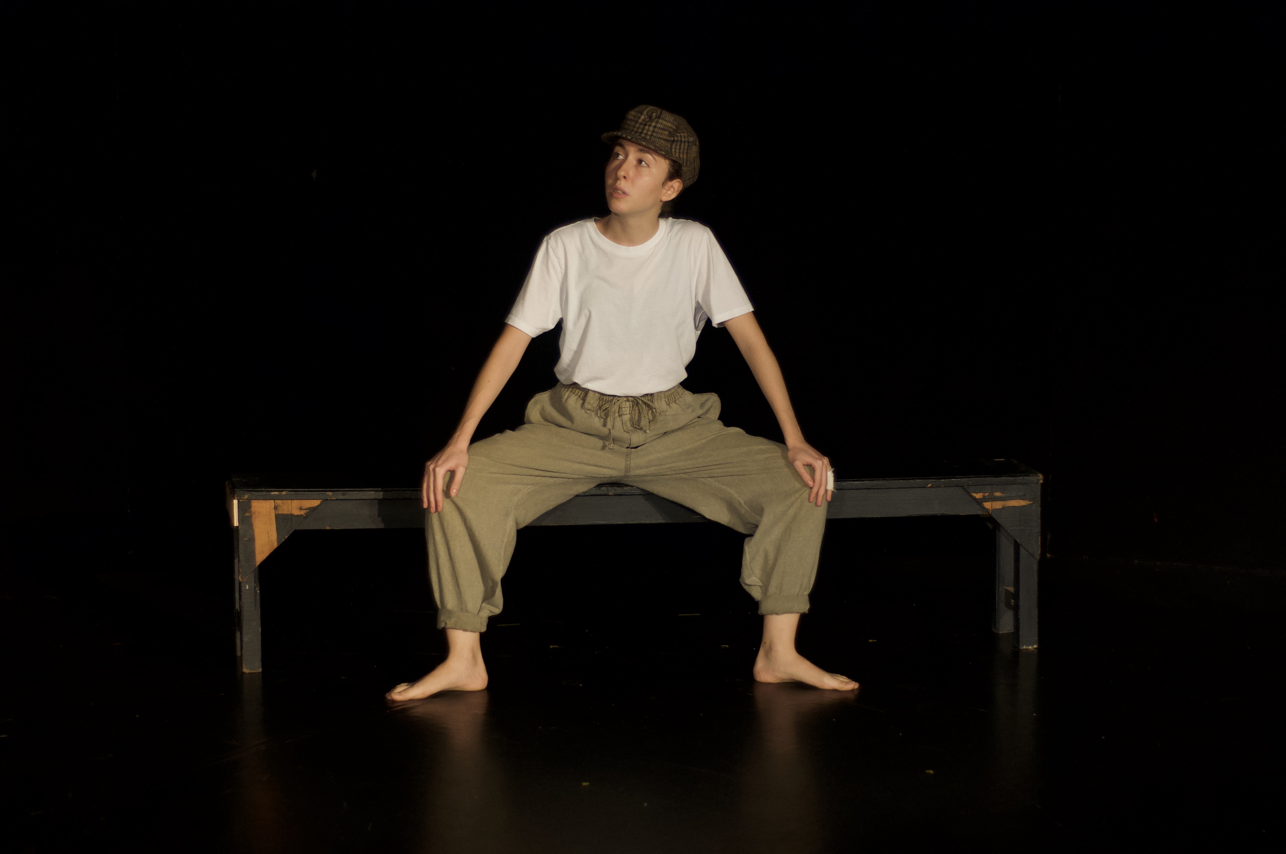 Giorgia sat on bench, wearing a newsboy cap, storytelling on stage